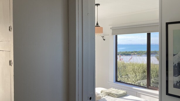 Une chambre avec un lit, une petite table et une vue sur la mer grâce à de grandes fenêtres.