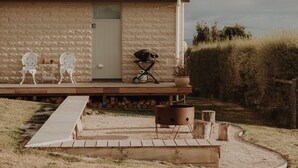 Il s’agit d’un bâtiment rustique doté d’un toit en métal, d’une terrasse en bois et d’un petit espace extérieur aménagé avec deux chaises et une table.