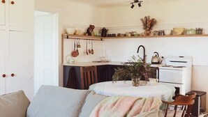 Une cuisine chaleureuse avec une table à manger, un porte-ustensiles suspendu et une cuisinière.