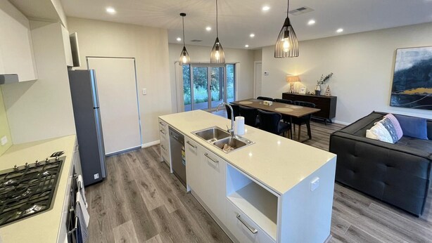 A modern kitchen with a central island, a dining area with a table and chairs, and a sofa in a living area. - Kesehills Wines Villa (Mount Pleasant)