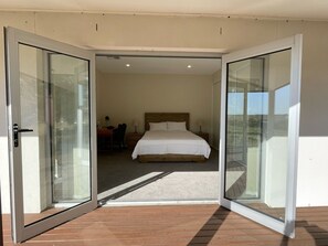 A bedroom with a bed, a desk, and a chair, connected to a balcony with a wooden floor. - Kesehills Wines Villa (Mount Pleasant)