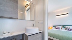 A modern bathroom with a round sink, a mirror, and a bedside table with a towel.