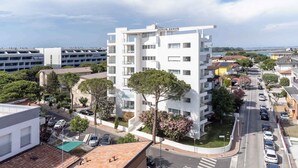 A modern multi-story hotel with a white facade, located in a coastal urban area with visible greenery and parked cars.