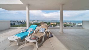 A balcony with two sun loungers, one with a blue cover and the other with a beige cover, and a woven mat on the floor.