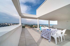 A rooftop terrace with a table set for two, white chairs, and a view of the city and sea. - Holiday apartment mit Klimaanlage und Balkon (Lignano)