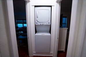Une petite buanderie blanche, dotée d’un lave-linge et d’un sèche-linge encastrés, située dans un couloir donnant sur un espace de vie.