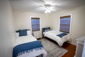 Een slaapkamer met twee bedden, een plafondventilator en een raam met zonwering.