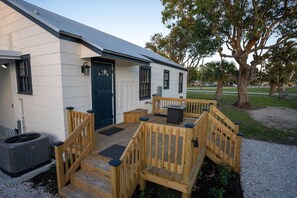 Un bâtiment avec une porte bleu foncé, une terrasse en bois dotée d’une rambarde et un panneau solaire sur le toit.
