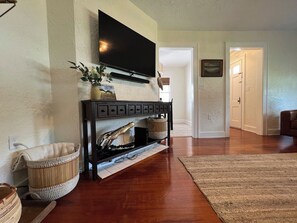 Een woonkamer met een flatscreen televisie aan de muur, een open haard met een schoorsteenmantel, een geweven mand en een vloerkleed op de houten vloer.