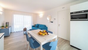 Una cucina moderna con microonde e forno, un'area pranzo con tavolo e sedie, un divano blu e una ciotola di frutta sul tavolo.
