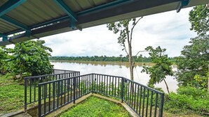 A covered outdoor area with a metal railing overlooking a calm body of water, surrounded by lush greenery. - OYO HOME 90682 Liliz Mambang Farmstay (Pekan)