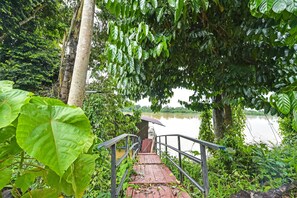 A wooden pathway leading to a small wooden structure by a lake, surrounded by lush greenery. - OYO HOME 90682 Liliz Mambang Farmstay (Pekan)