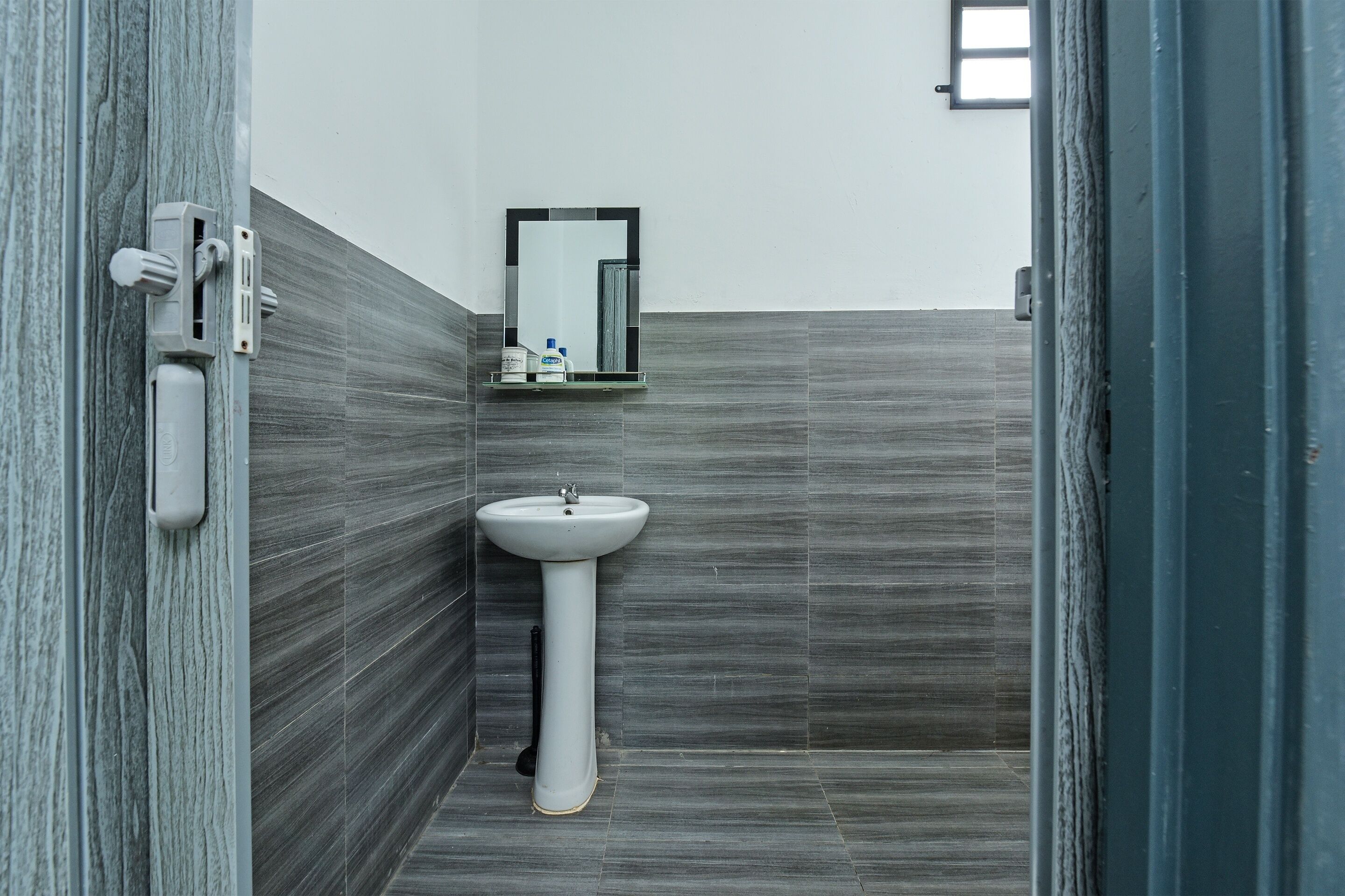 A bathroom with a pedestal sink, a mirror, and a shelf with toiletries.