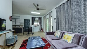 A modern living room with a sofa, a coffee table, and a TV. There is a kitchen in the background with a dining area. - OYO HOME 90682 Liliz Mambang Farmstay (Pekan)
