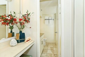 Une salle de bain équipée de toilettes, d’un lavabo et d’un porte-serviettes. On peut y voir deux vases ornés de fleurs rouges, posés sur le comptoir.