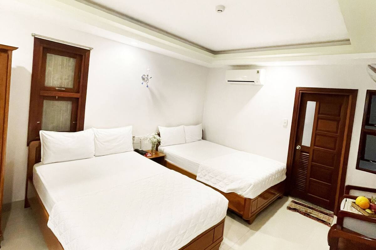A hotel room with two single beds, a wooden wardrobe, a wooden desk, and a small table with fruit.