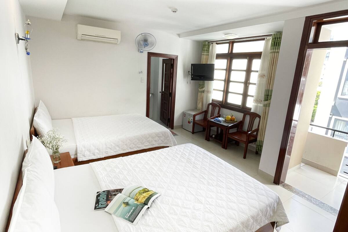A hotel room with two beds, a TV, an air conditioner, and a balcony with a table and chairs.
