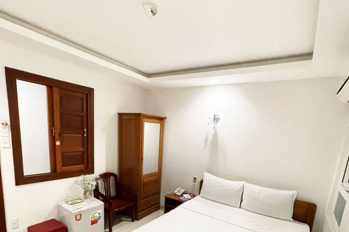 A bedroom with a large bed, a wooden wardrobe, a small table, and a mirror on the wall.