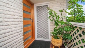 Une porte avec un cadre en bois et un moustiquaire, un mur en briques blanches et un pot de fleurs sur un balcon.
