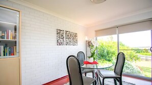 Un espace repas avec un mur en briques blanches, une bibliothèque et une vue sur la verdure à l’extérieur.