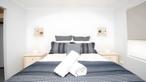 Un lit bien fait, recouvert d’une couvre-lit à motifs, deux tables de chevet avec des lampes et deux œuvres d’art accrochées au mur.