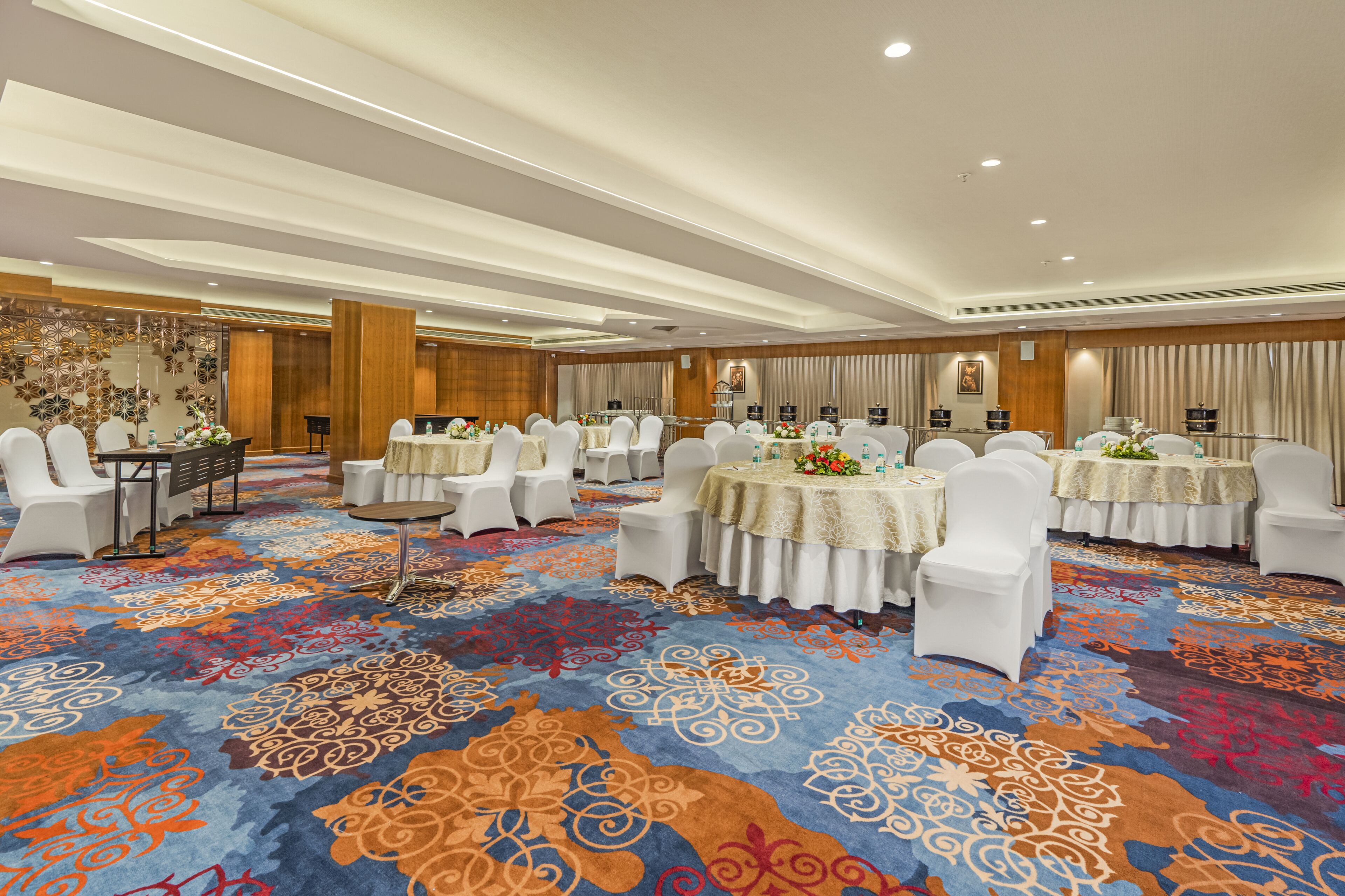A hotel conference room with multiple round tables, white chairs, and a patterned carpet.