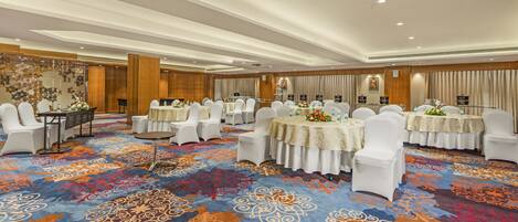 A hotel conference room with multiple round tables, white chairs, and a patterned carpet.