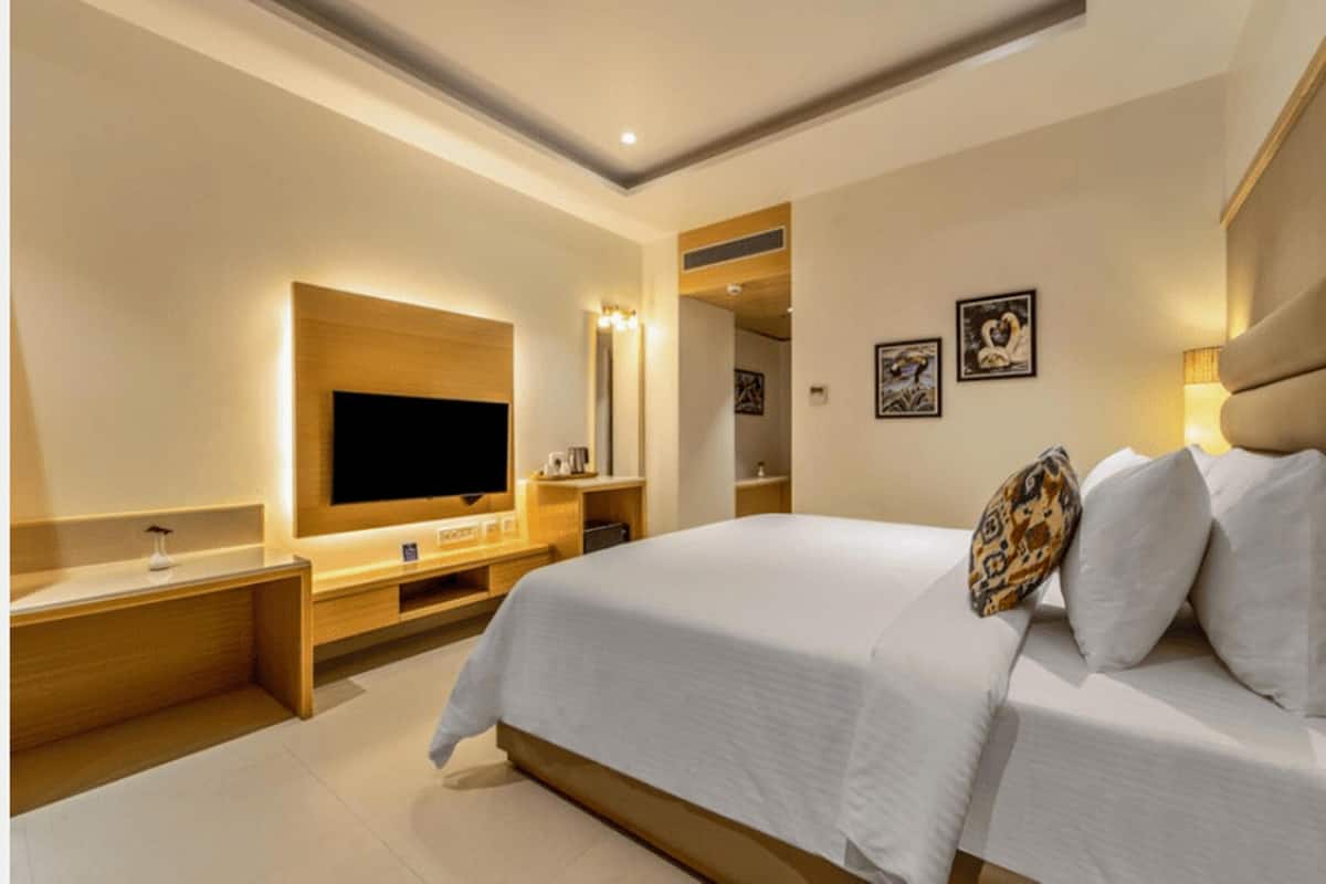 A modern hotel room with a large bed, a flat-screen TV, a wooden console table, and a mirror.