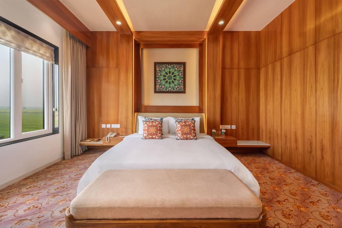 A hotel room with a large bed, wooden paneling, a view of the outdoors, and a decorative wall piece.