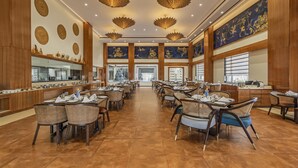 Un vaste espace dédié à la salle à manger, avec de nombreuses tables et chaises, une allée centrale et des luminaires décoratifs au plafond.