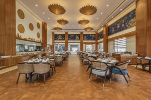 Un amplio comedor con varias mesas y sillas, un pasillo central y luminarias decorativas en el techo.