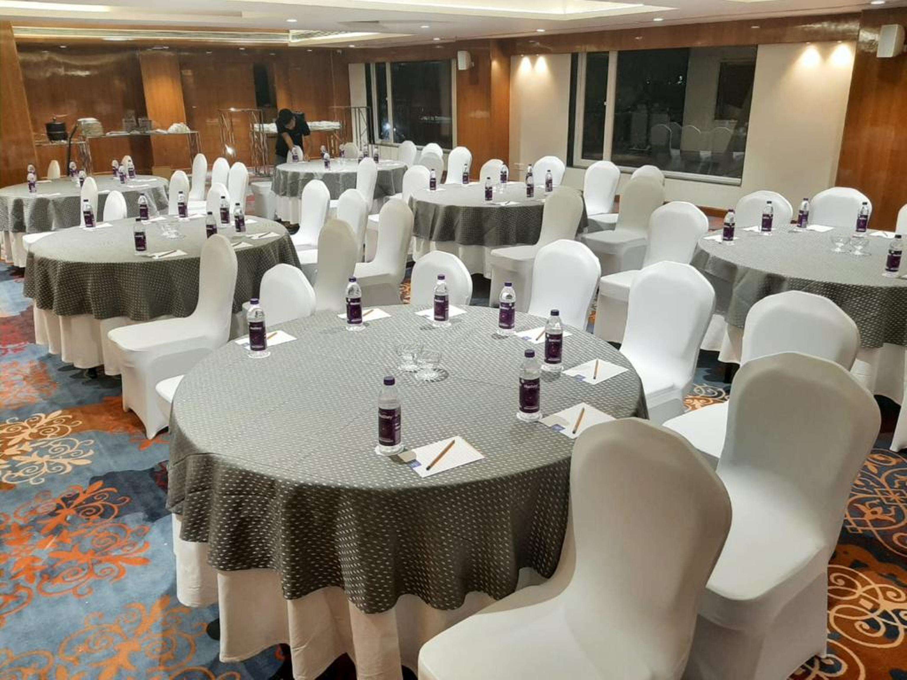 Un salón de conferencias con mesas redondas, sillas blancas y botellas de agua.