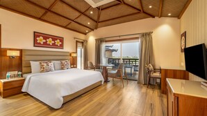 Une chambre d’hôtel avec un grand lit, un plancher en bois, un coin repas avec une table et des chaises, et un téléviseur posé sur un meuble.