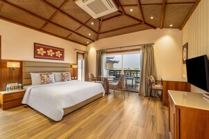 Habitación de hotel con una cama grande, suelo de madera, zona de comedor con mesa y sillas, y un televisor sobre un mueble.