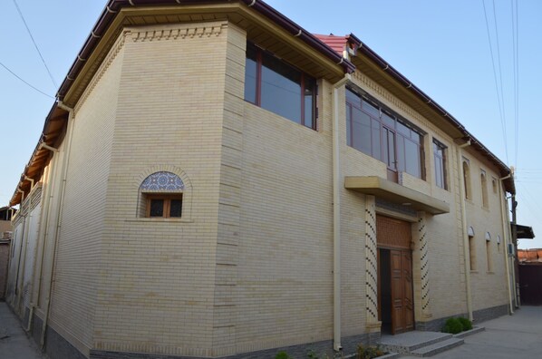 A two-story building with a tiled facade, a small window with a decorative design, and a wooden door. - El Emir Samarkand (Samarkand)