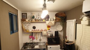 Une cuisine compacte équipée d’un évier, d’un four à micro-ondes, d’une machine à café et d’un réfrigérateur. On y trouve des étagères remplies de divers ustensiles de cuisine et une fenêtre dotée d’un cadre bleu.