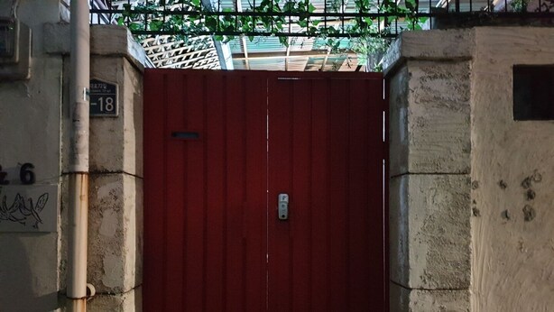 Une porte rouge dotée d’un clavier pour l’ouverture, un mur en béton avec une plaque portant un numéro, et un tuyau en métal.