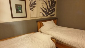 Une chambre avec deux lits simples, une œuvre d’art encadrée au mur et une grande tapisserie ornée de motifs de feuilles.