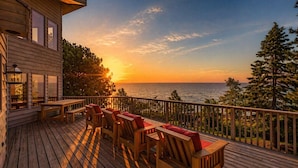 Una terraza de madera con mobiliario exterior, con vista a la puesta de sol sobre el océano.