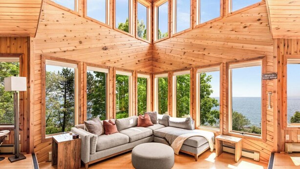 Una cabaña de troncos moderna con un amplio salón que cuenta con un sofá seccional, reposapiés y vistas al lago.