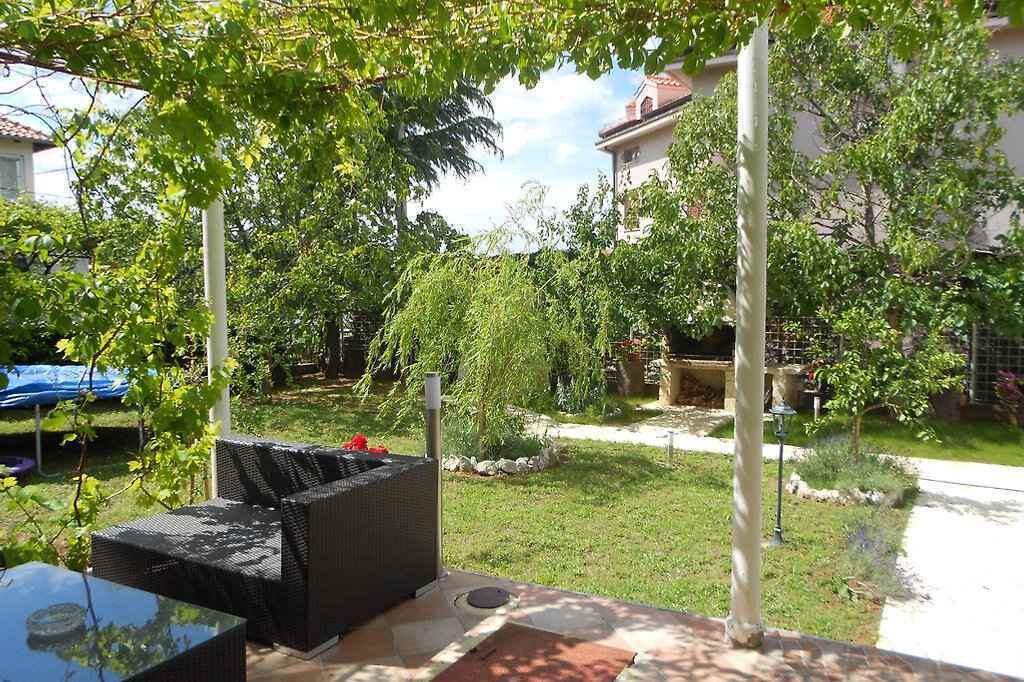 Een terras met rieten meubels, een kleine tuin en een gebouw op de achtergrond.