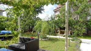 A patio with wicker furniture, a small garden area, and a building in the background. - Holiday home 50 meters from the meter with large garden (Sukošan)