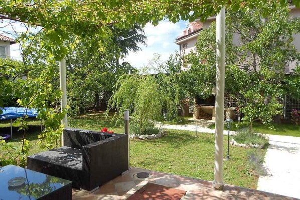 A patio with wicker furniture, a small garden area, and a building in the background.