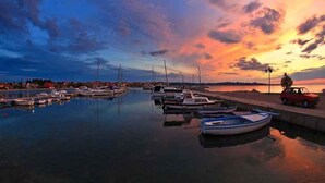 A marina with boats docked, a car parked on the side, and a sunset in the background. - Holiday home 50 meters from the meter with large garden (Sukošan)