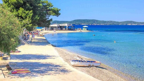A beach with clear blue water, a boat on the shore, and people enjoying the area. - Holiday home 50 meters from the meter with large garden (Sukošan)