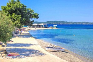 A beach with clear blue water, a boat on the shore, and people enjoying the area.