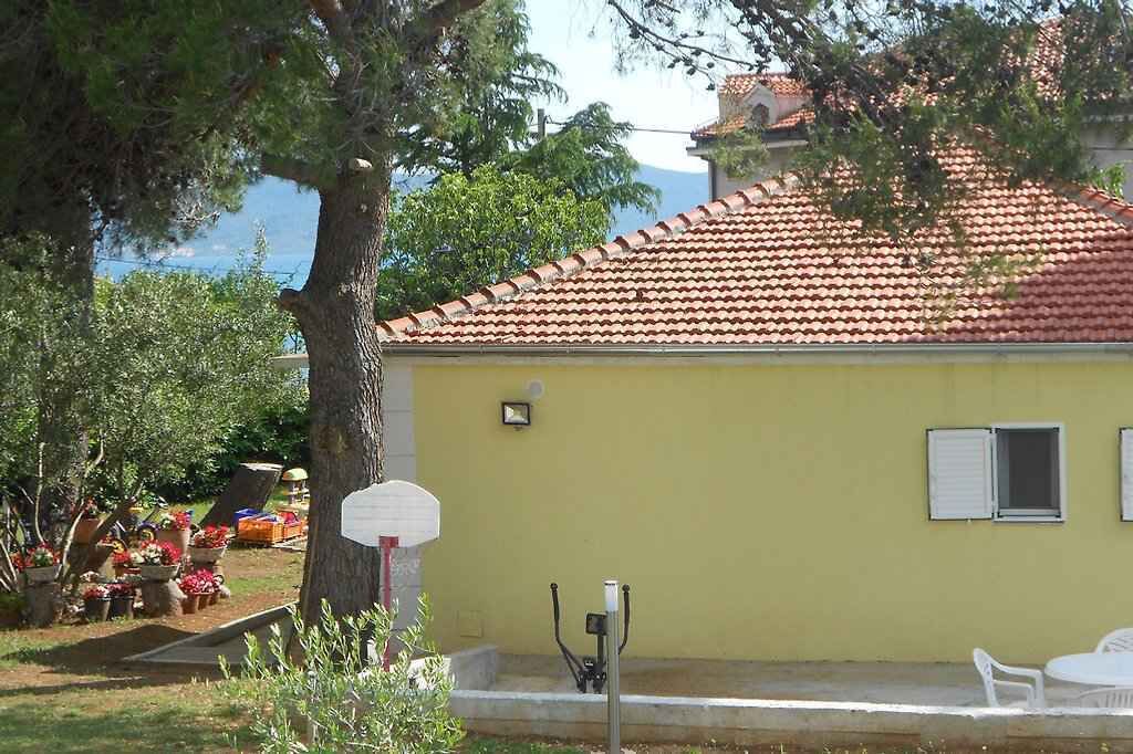 Um edifício amarelo com telhado de telhas vermelhas, um cesto de basquete e área de estar externa.