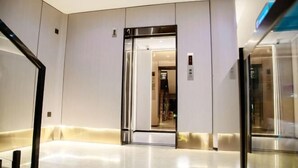 En moderne elevator med metallisk overflade og glasdøre, der fører til et godt oplyst rum indeni.