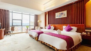 A hotel room with two beds, a desk, and a large window offering a city view. - Guowei Hotel (Menghai)