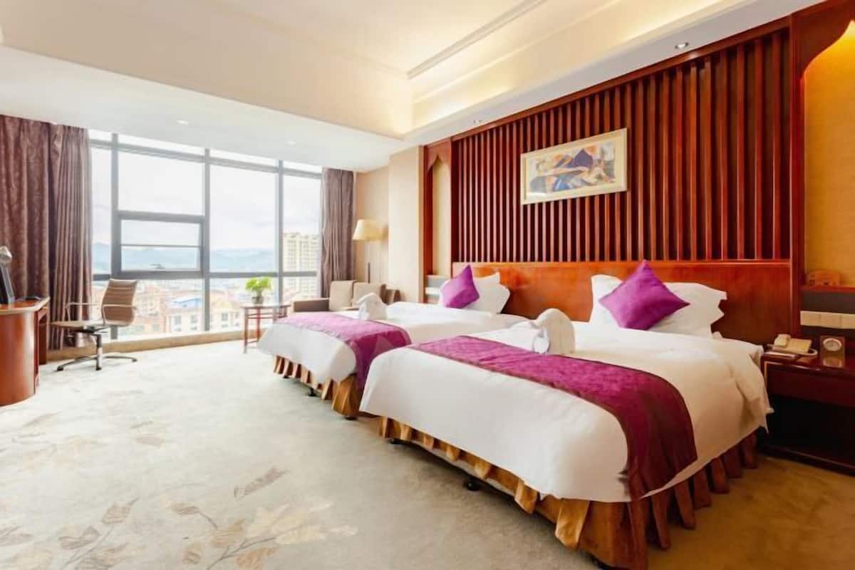 Habitación de hotel con dos camas, un escritorio y un ventanal grande con vistas a la ciudad.